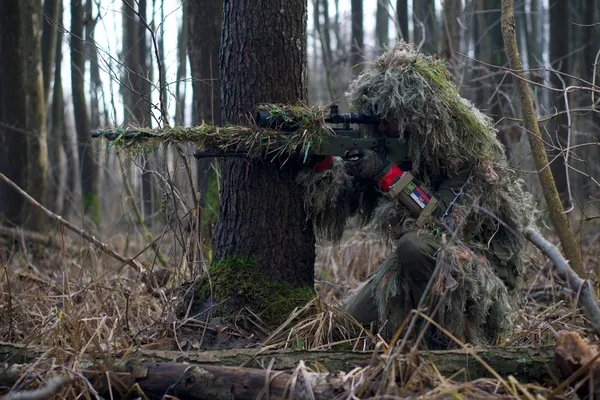 Camouflaged sniper aiming from a forest hideout