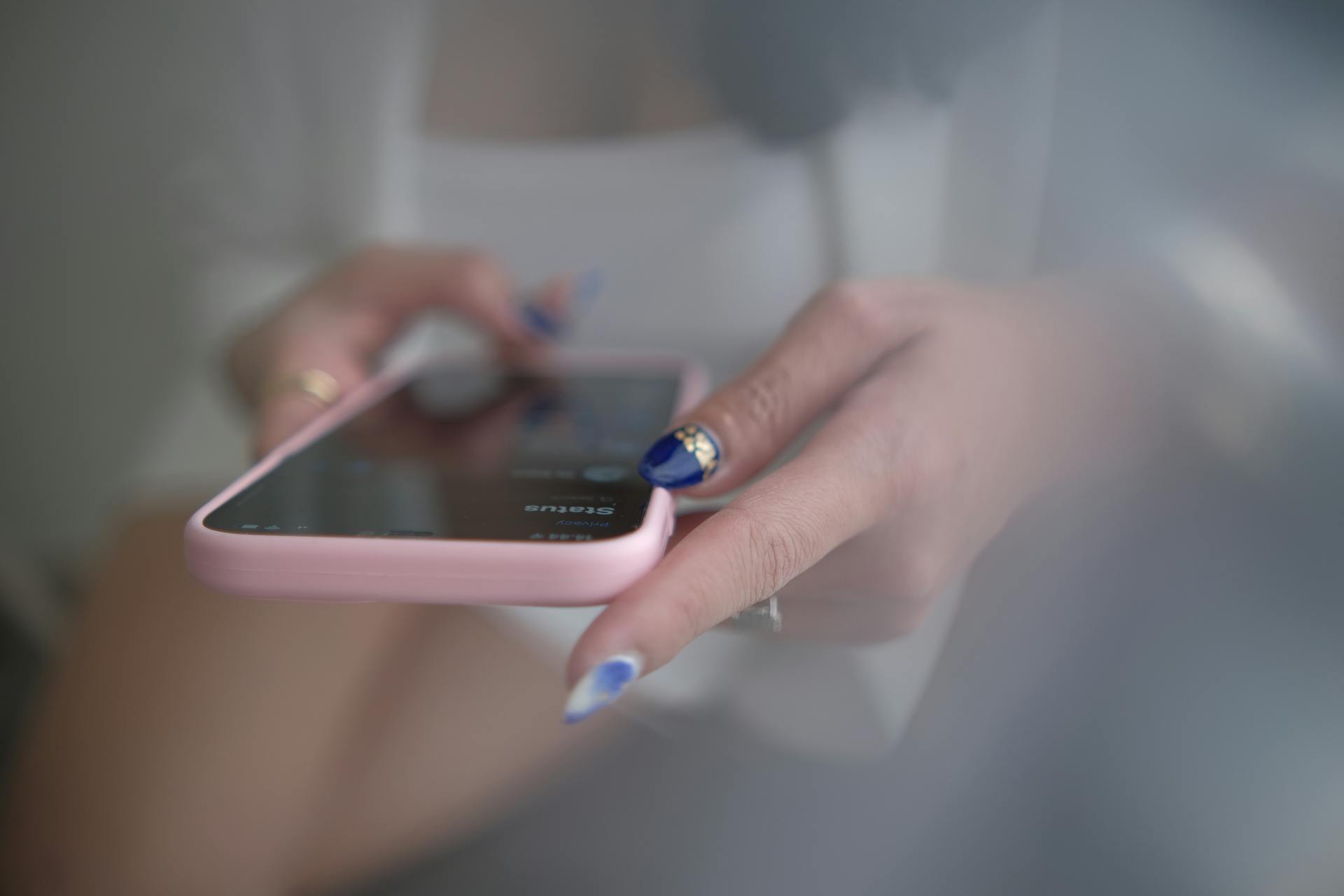 Close-up of hands with deep blue nail art holding a pink-cased smartphone.