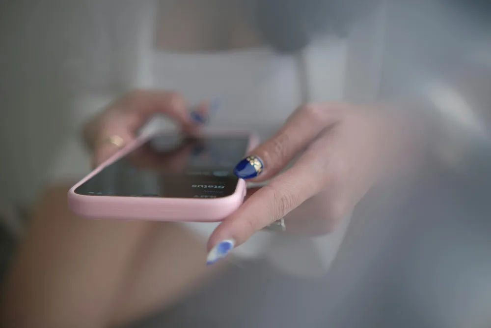 Nahaufnahme von Händen mit tiefblauem Nagellack, die ein Smartphone mit pinker Hülle halten.